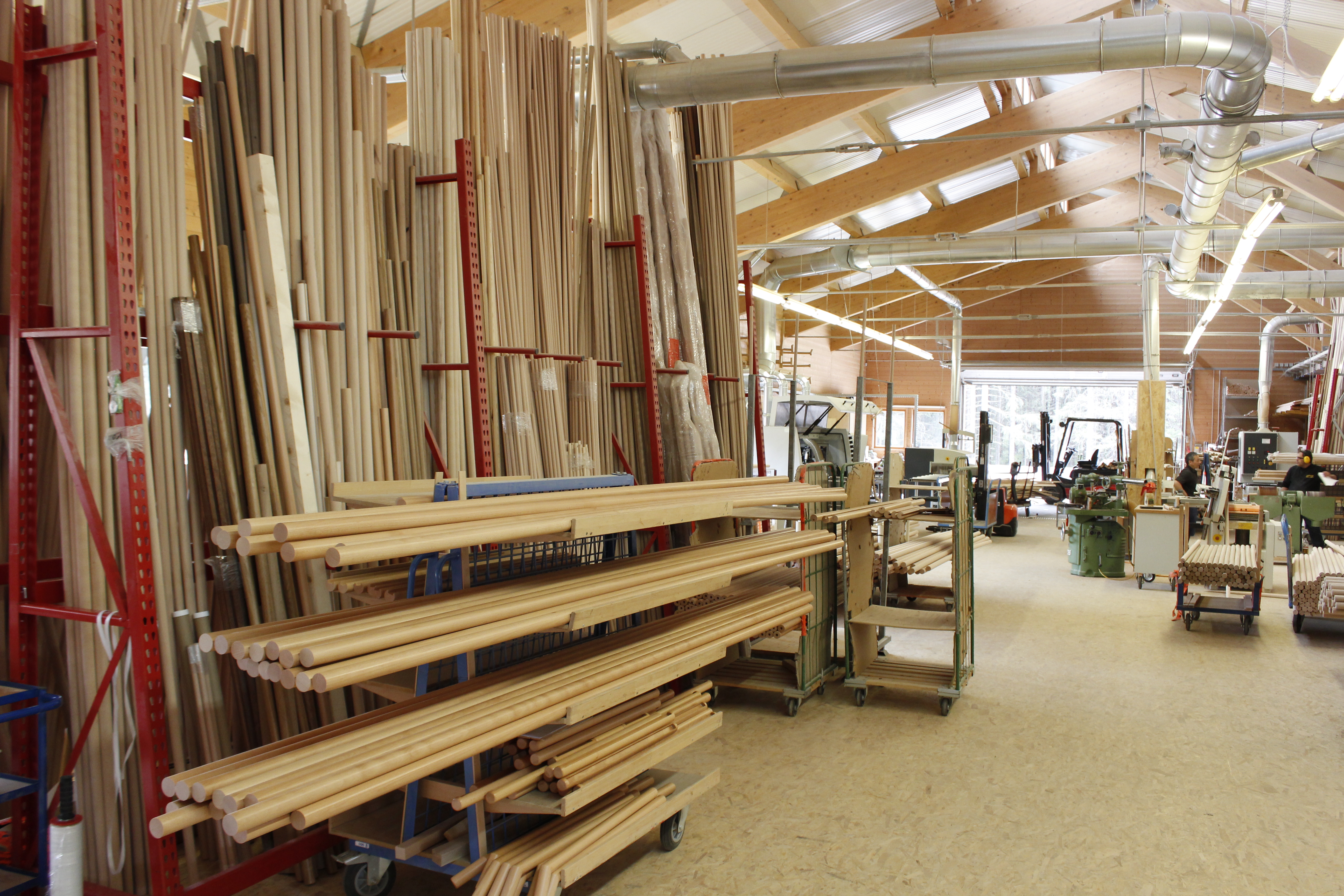 Houten leuningen en ronde staven in het magazijn van de draaierij, lange staven in rode draagarmstellingen in de werkhal