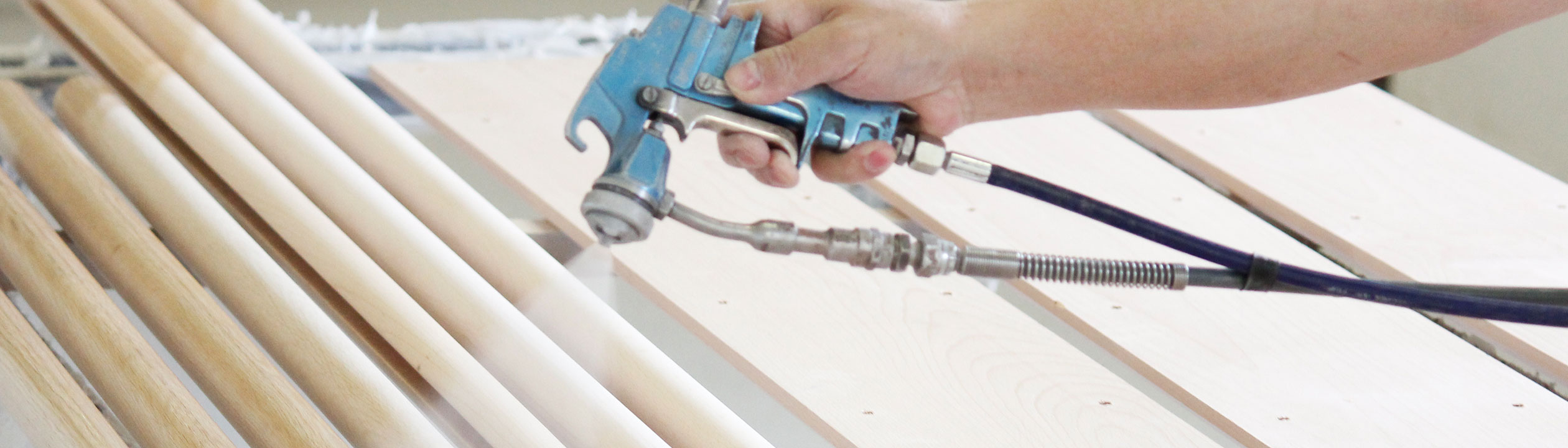 Leuningproductie: houten leuningen worden met het spuitpistool gelakt, hand met spuitpistool boven lichte houten staven