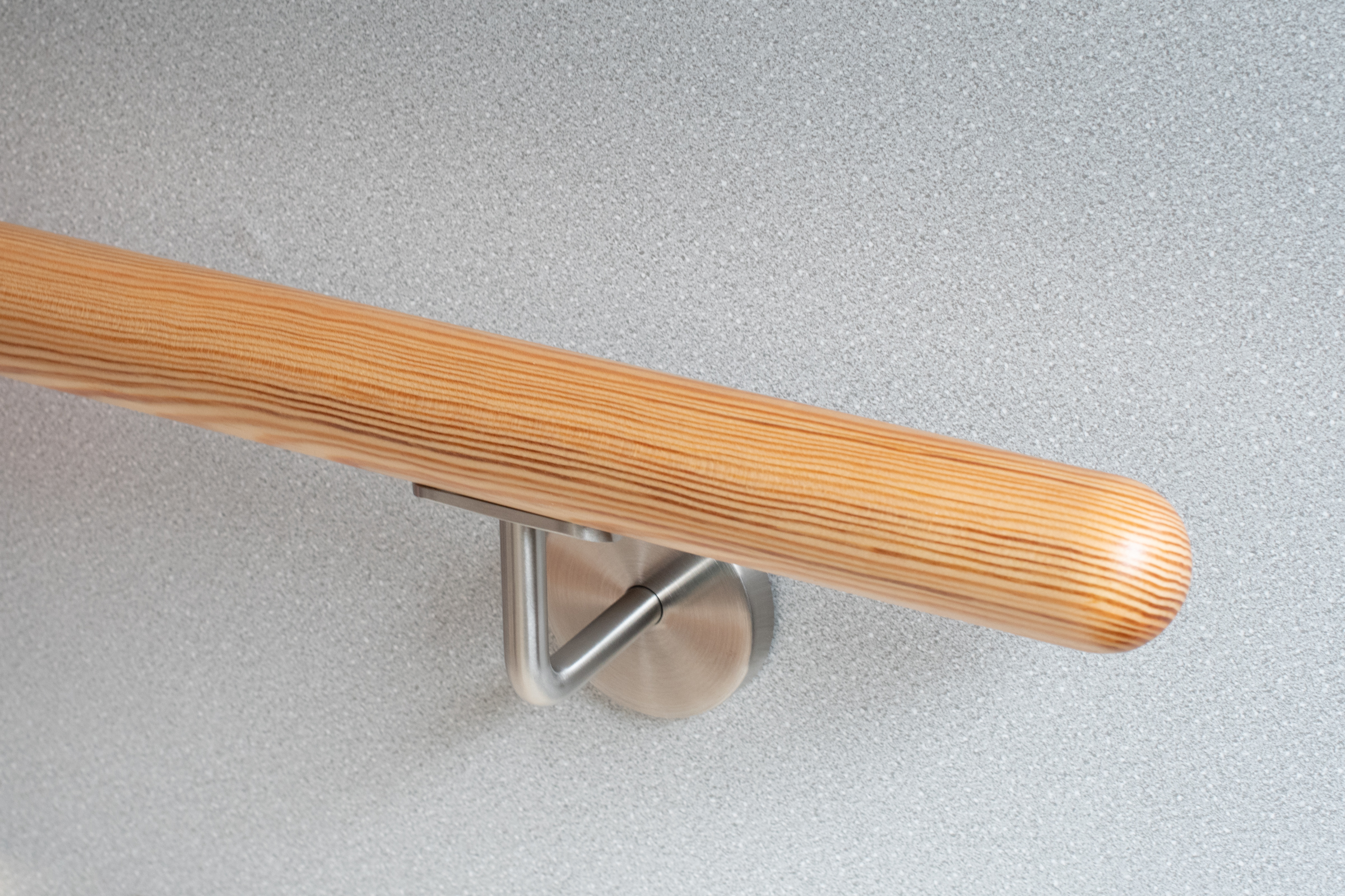 Ronde leuning van grenenhout met roestvrijstalen wandhouder voor lichtgrijze wand, naaldhout met zichtbare nerf, close-up