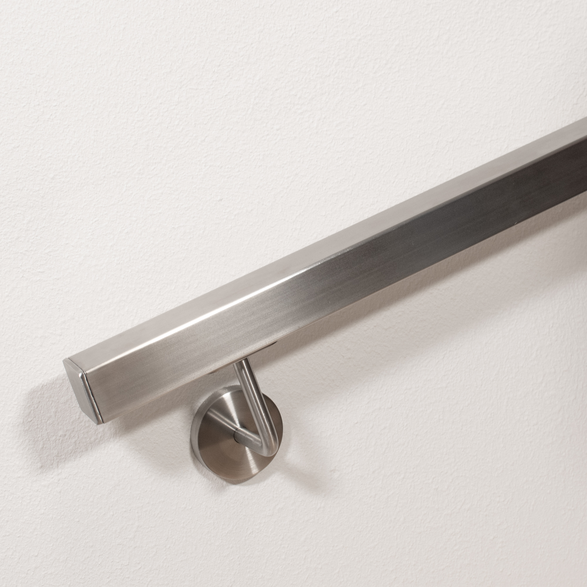 Vierkante roestvrijstalen leuning met vlakke eindkap en gebogen wandhouder, leuningeinde in detail aan witte wand