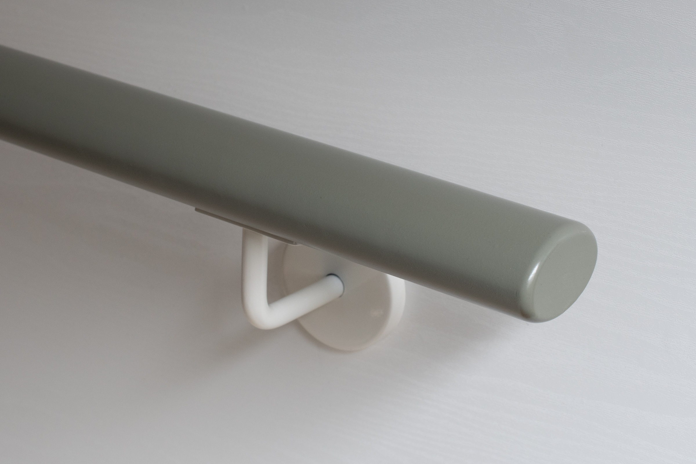 Ronde houten leuning, grijs gelakt, met wit gelakte wandhouder aan witte wand, close-up van het ronde uiteinde