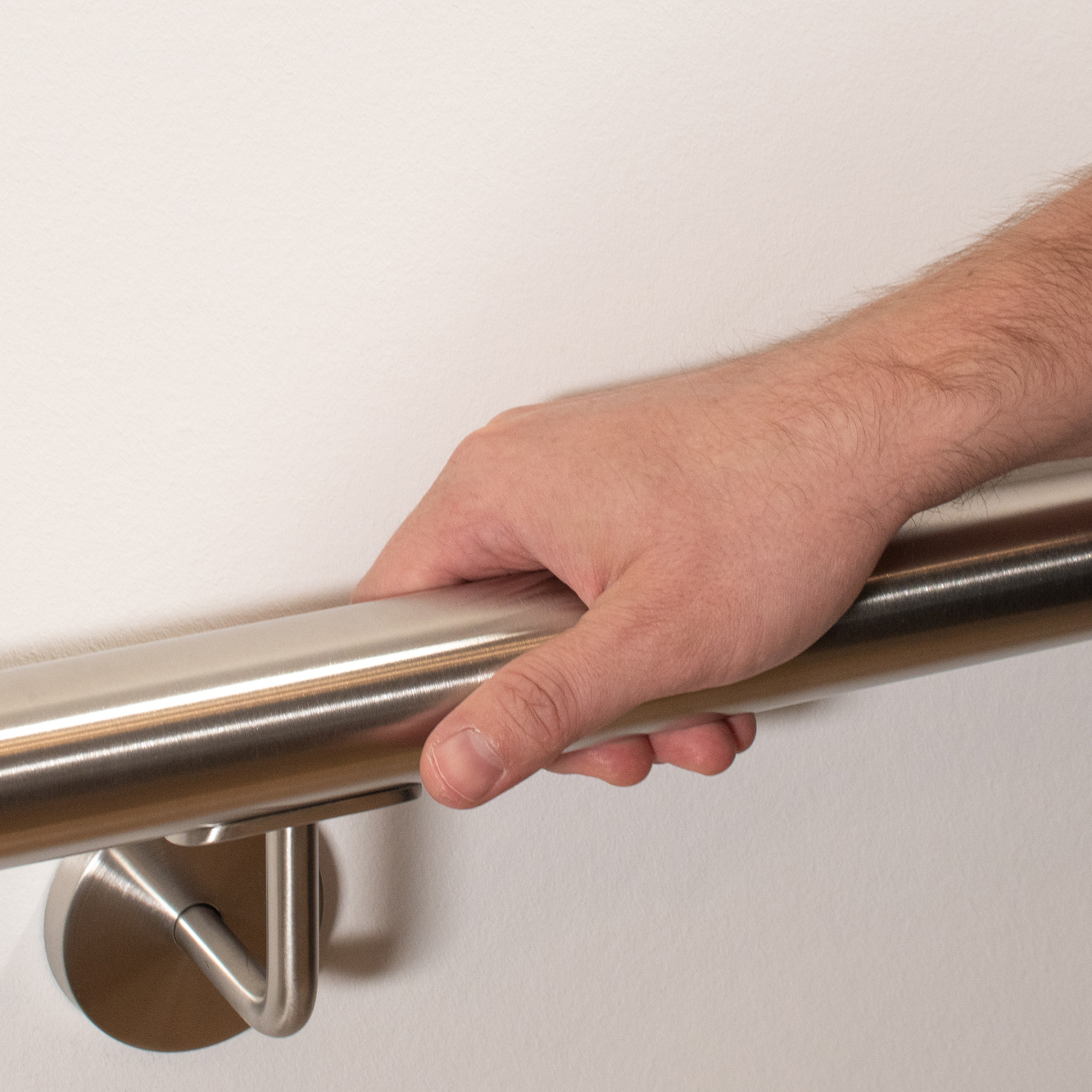 Ronde roestvrijstalen leuning aan witte wand met roestvrijstalen leuninghouder, hand omvat de leuning, close-up