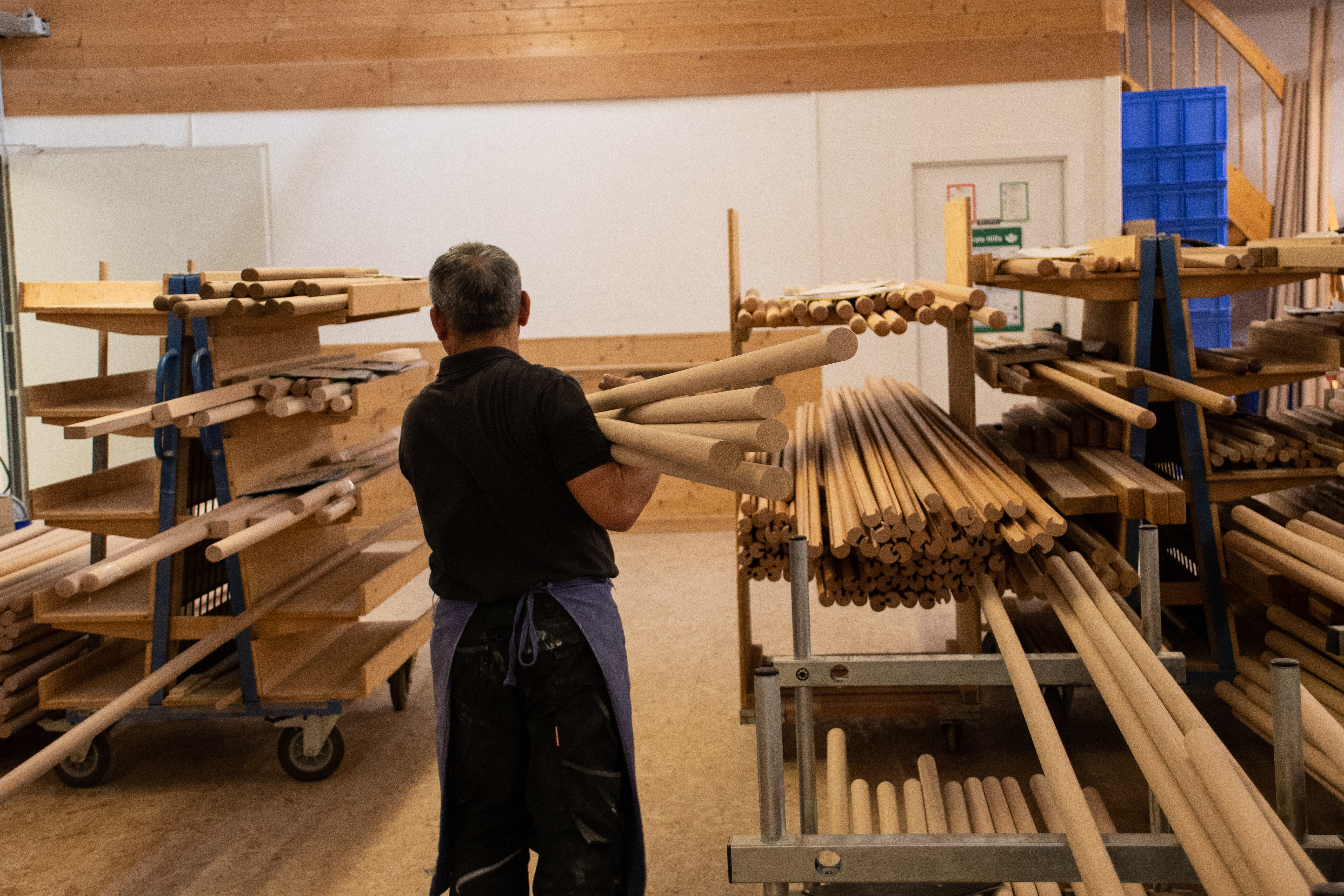 Ronde houten staven in het werkplaatsrek, medewerker sorteert houten staven in de draaierij, veel verschillende diameters
