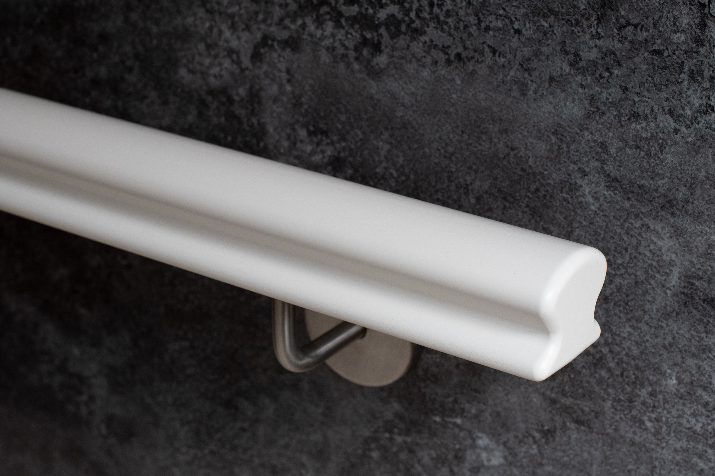 Wit gelakte houten Omega-leuning met roestvrijstalen wandhouder voor donkergrijze wand, close-up van het profiel