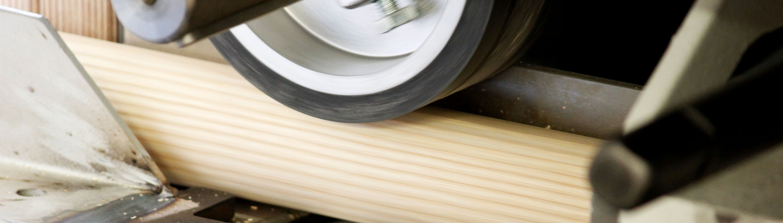 Leuningproductie: houten ronde staaf wordt in de schuurmachine geschuurd, close-up van de schuurwals, bannerformaat
