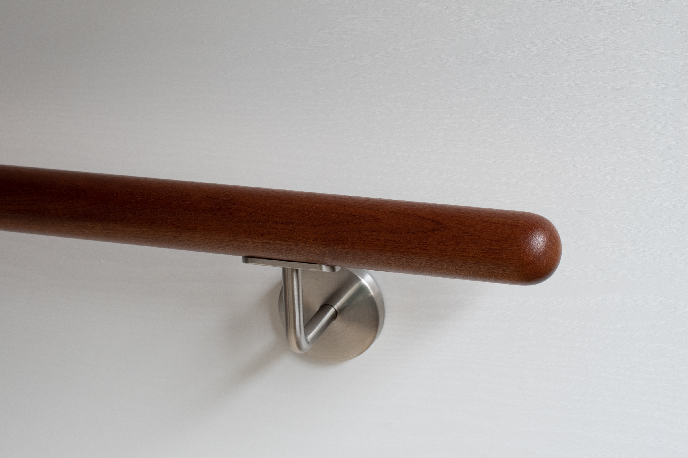 Ronde leuning van mahoniehout met roestvrijstalen wandhouder aan witte wand, roodbruin hout, close-up van het afgeronde eind