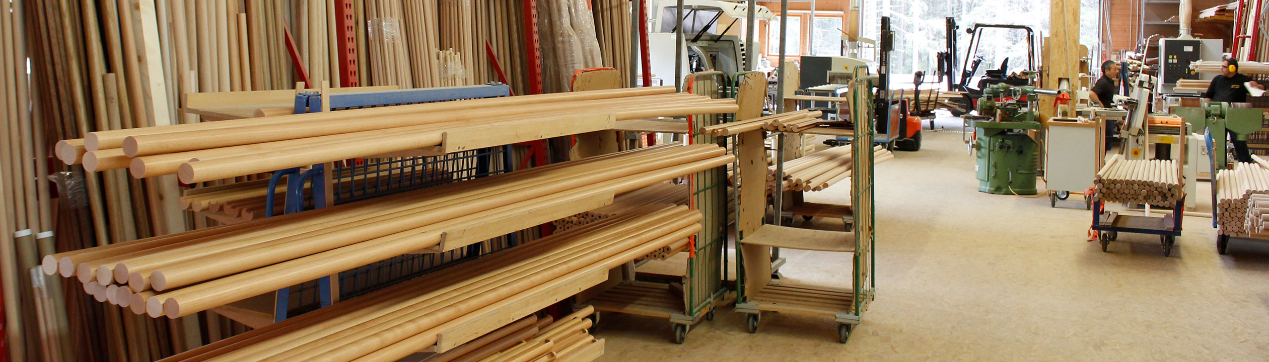 Leuningproductie: magazijn met lichte houten leuningen en ronde staven op rolwagens in de werkplaats, bannerformaat
