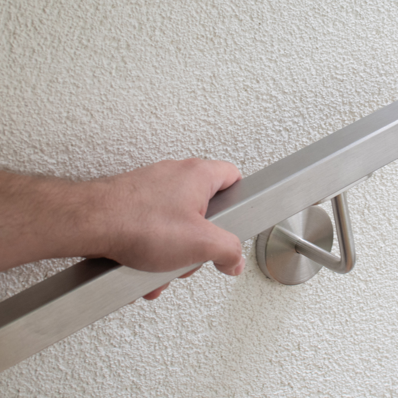 Vierkante roestvrijstalen leuning aan gepleisterde wand, hand omvat de leuning, roestvrijstalen wandhouder met rozet