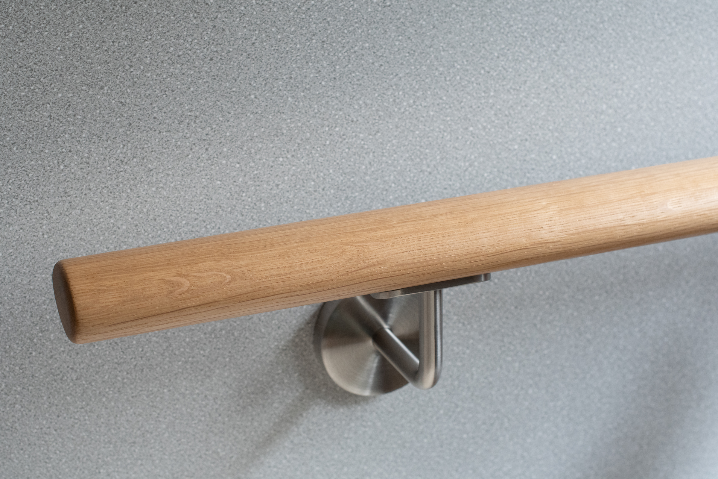 Ronde leuning van eikenhout met roestvrijstalen wandhouder voor lichtgrijze wand, close-up met duidelijke eikennerf