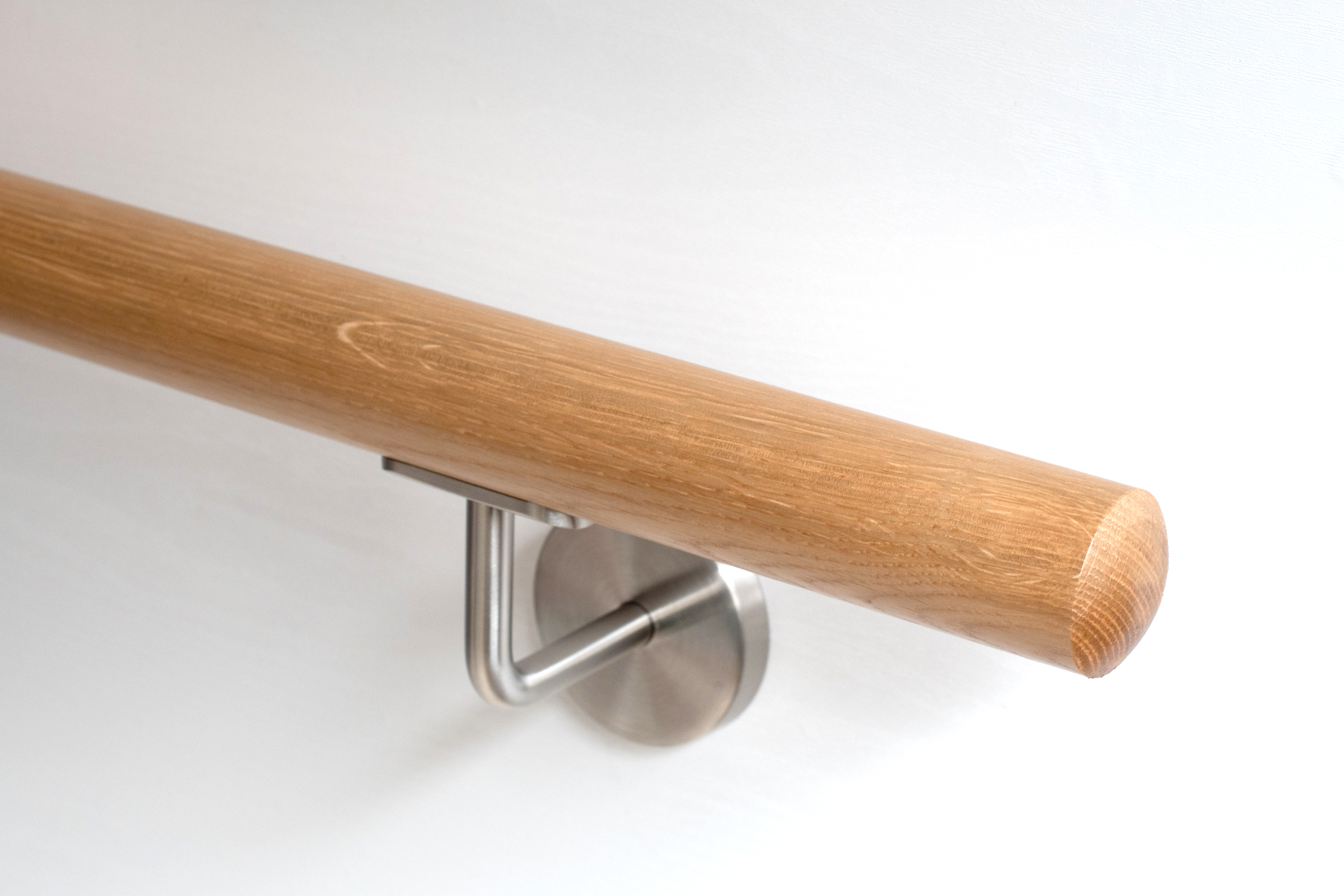 Ronde leuning van rood eikenhout met roestvrijstalen wandhouder aan witte wand, close-up van het afgeronde uiteinde met nerf