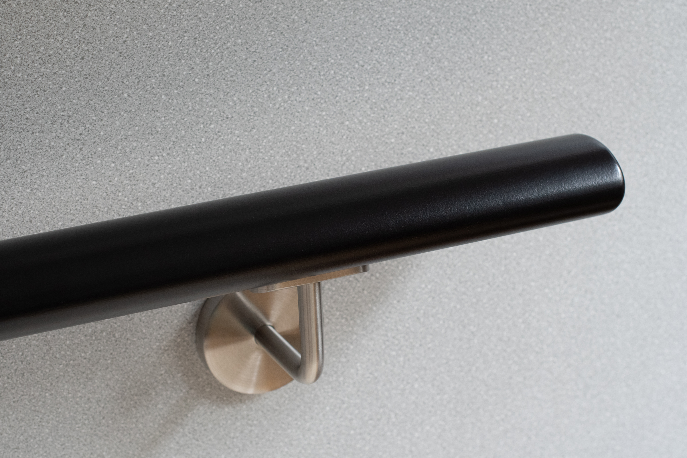 Ronde houten leuning, zwart gelakt, met roestvrijstalen wandhouder voor grijze wand, close-up van het afgeronde uiteinde