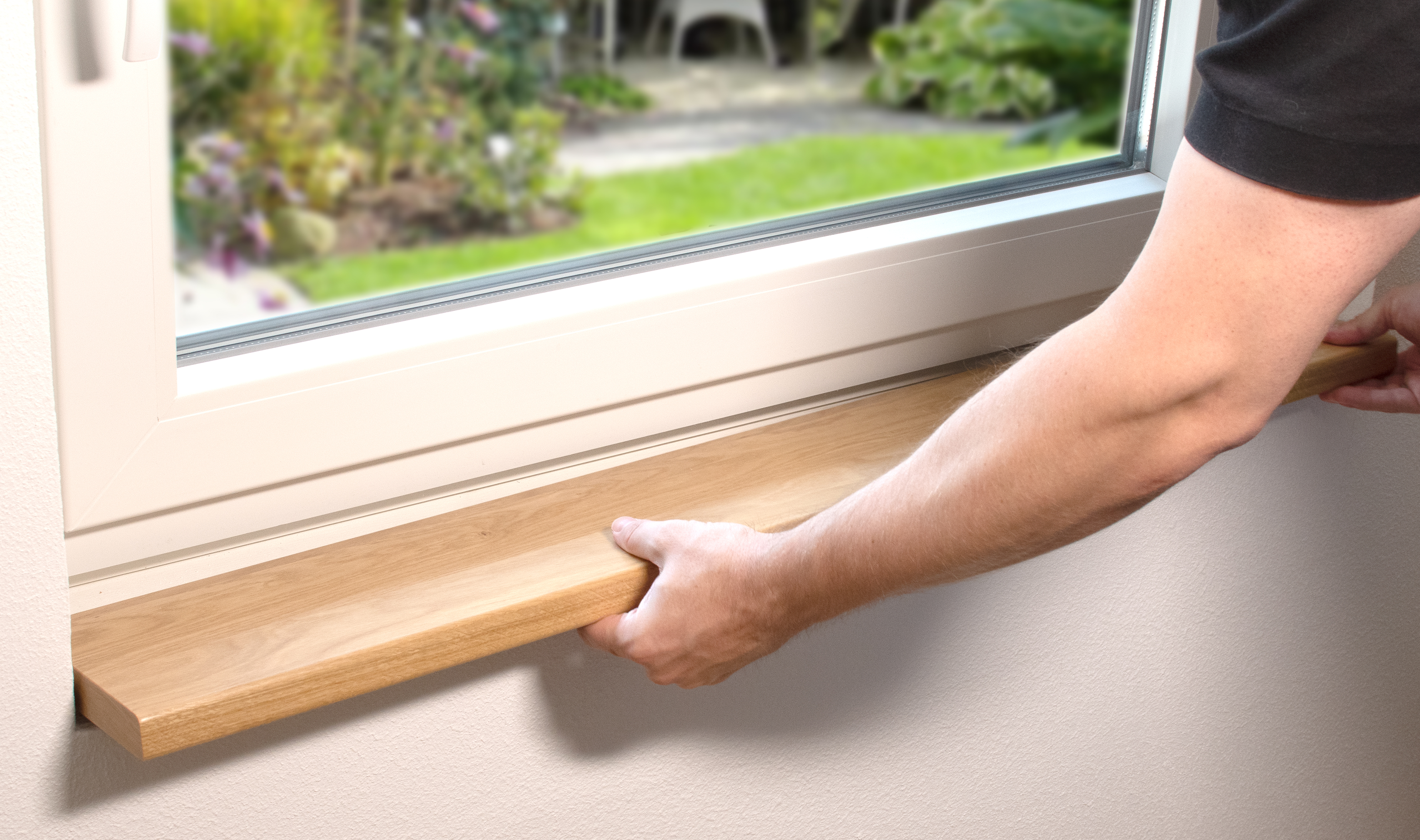 Vensterbank van massief hout bij de inbouw: hand plaatst lichte houten vensterbank onder wit raam, uitzicht op de tuin